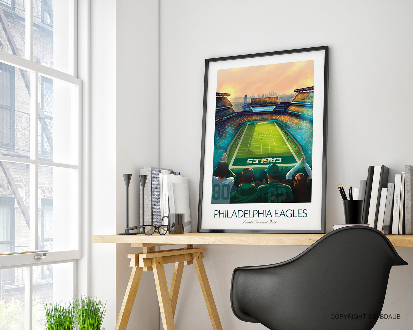 Framed Philadelphia Eagles stadium poster on a home office desk with a chair and books in a bright room.