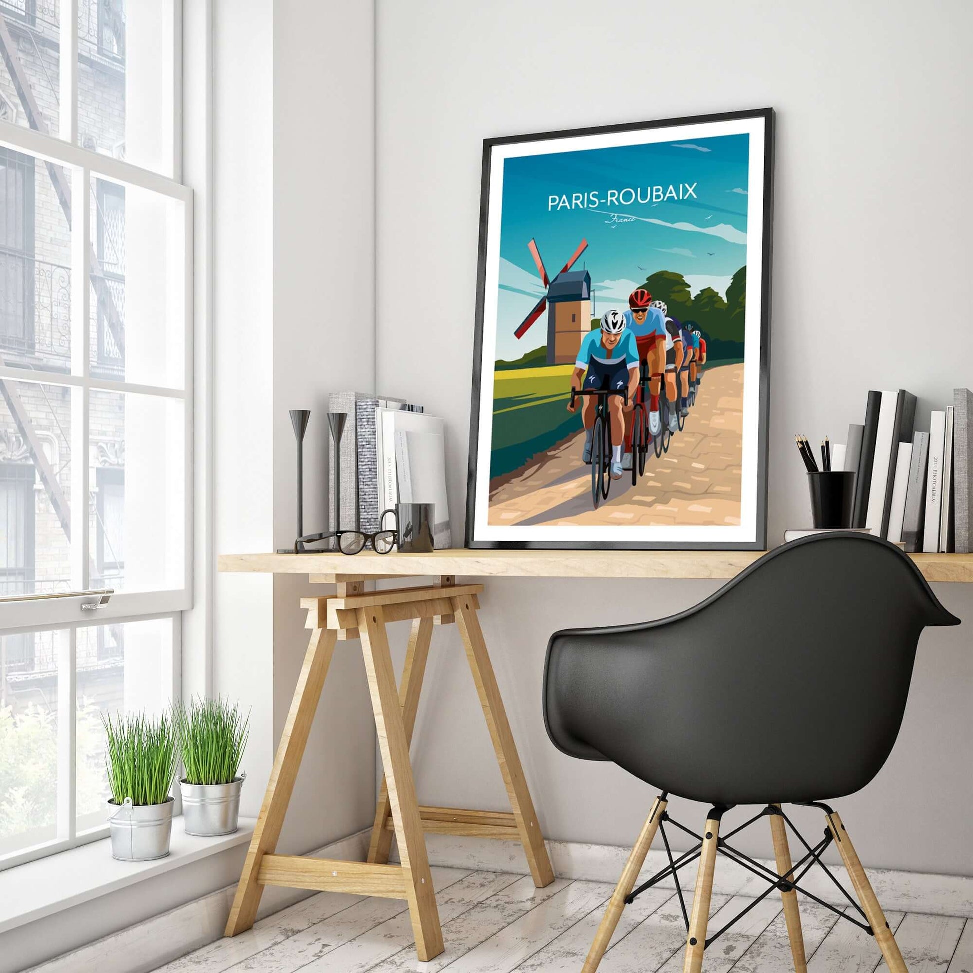 Large and colourful cycling poster of Paris Roubaix, framed and displayed on a home office desk.