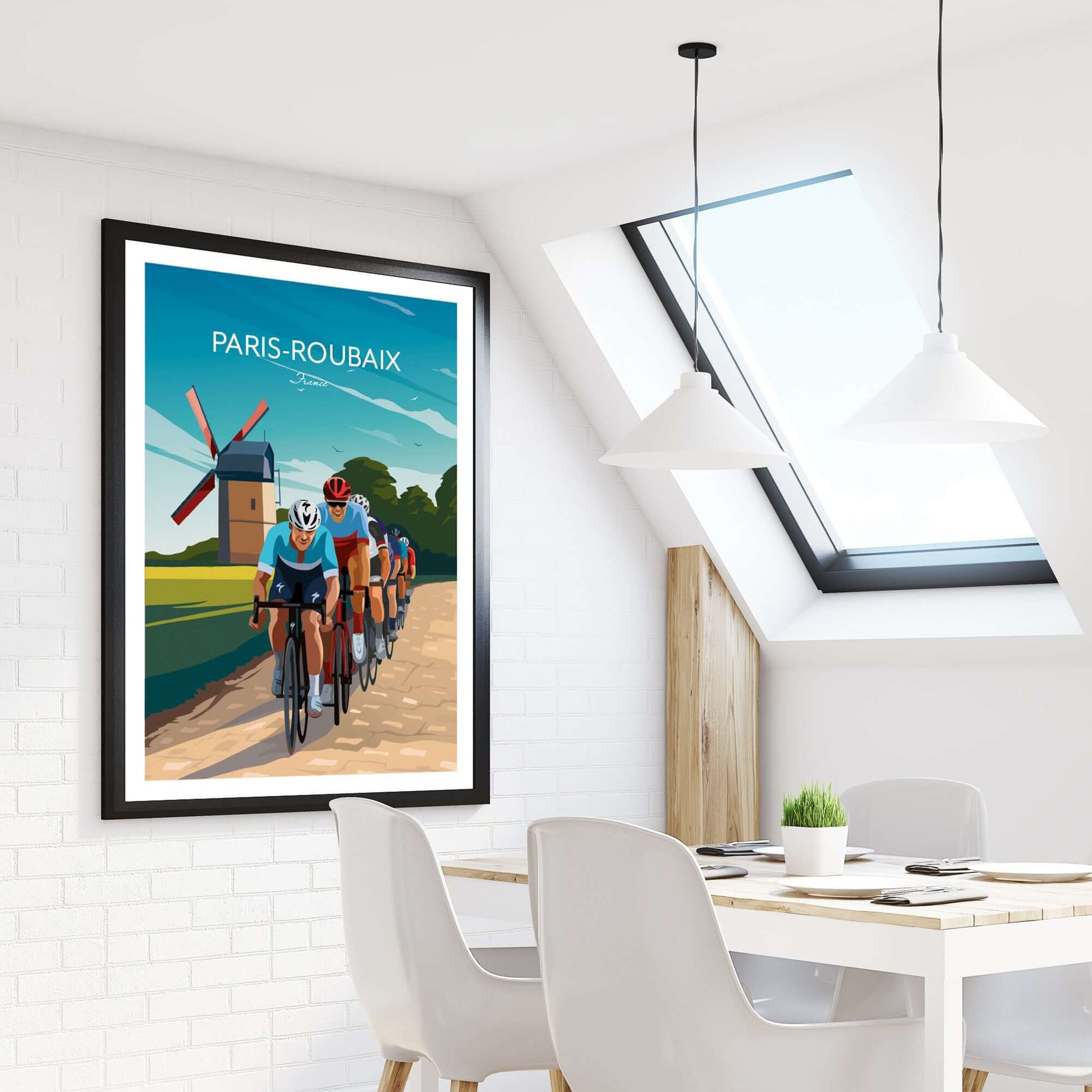 Colorful cycling art print of the Paris Roubaix Monuments race, displayed within a frame on an apartment wall beside a dining table and window.
