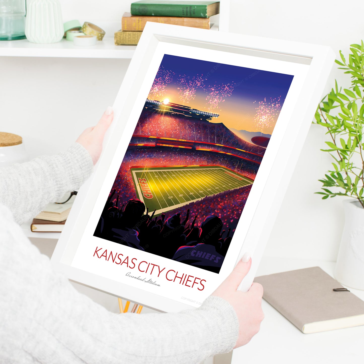 Framed artwork of a Arrowhead football stadium with 'Kansas City Chiefs' text, held by a person.