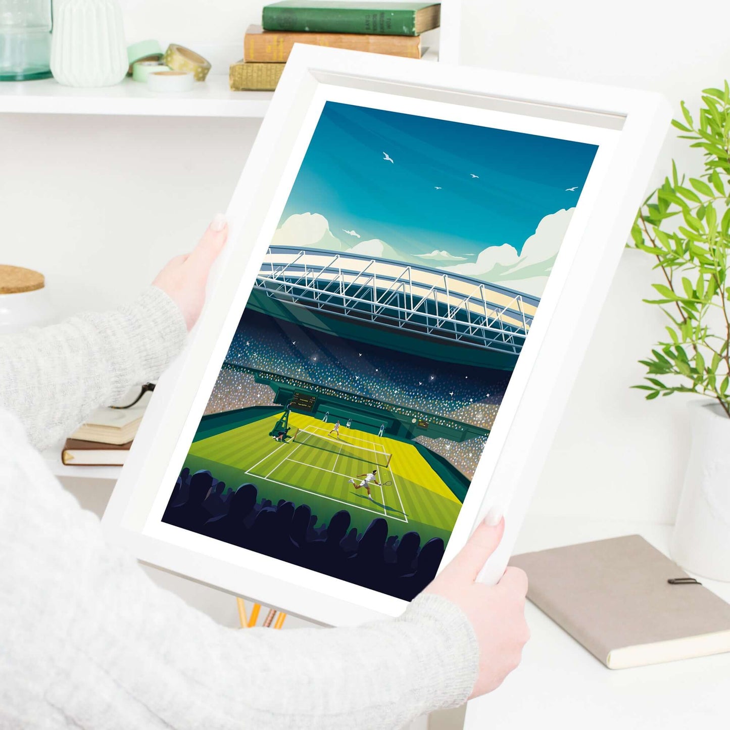 Tennis poster of Wimbledon in a white frame, being held by a woman in a living room.