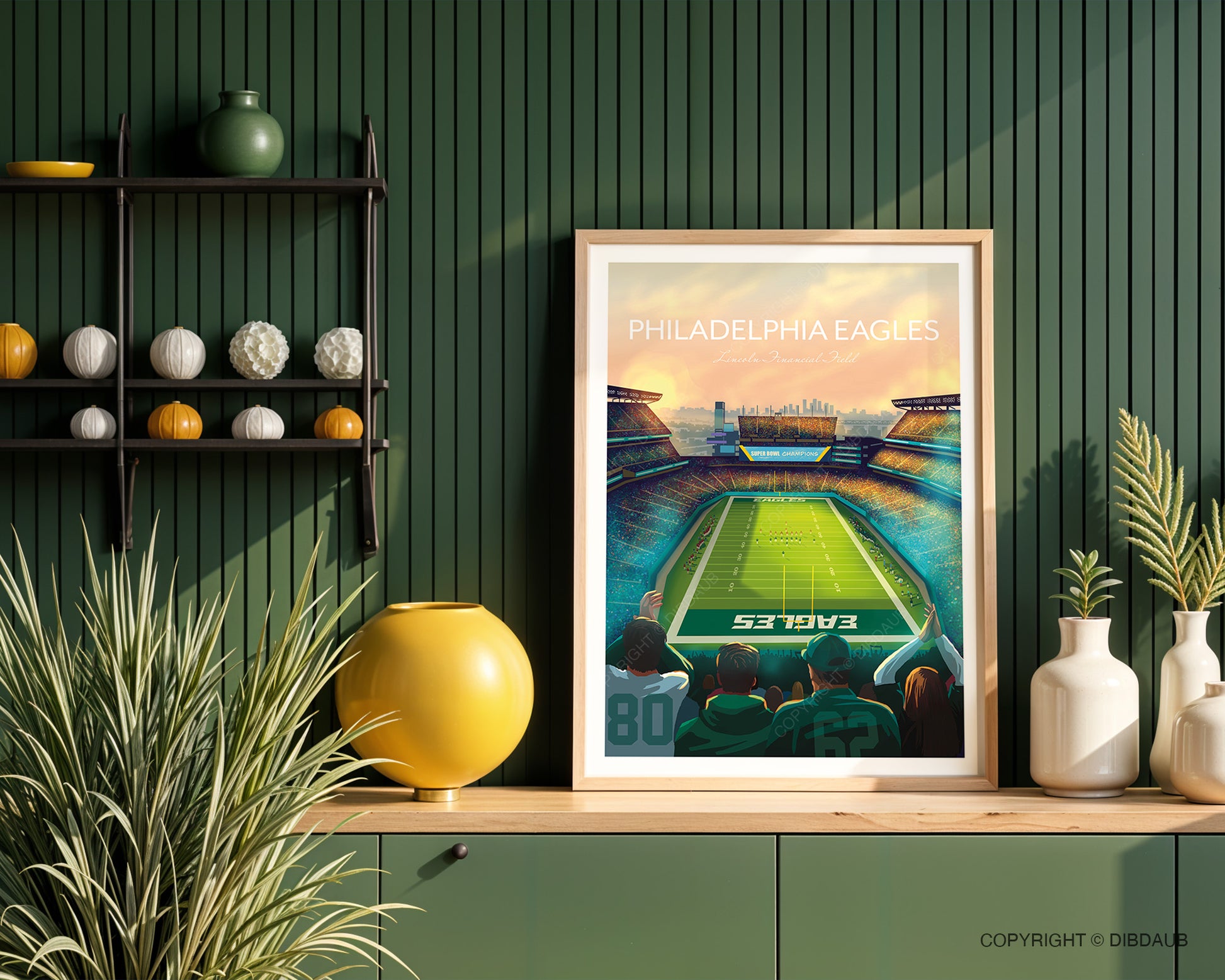 Framed art print of Philadelphia Eagles football stadium on a wooden worktop against a green wall with plants and ornaments either side.