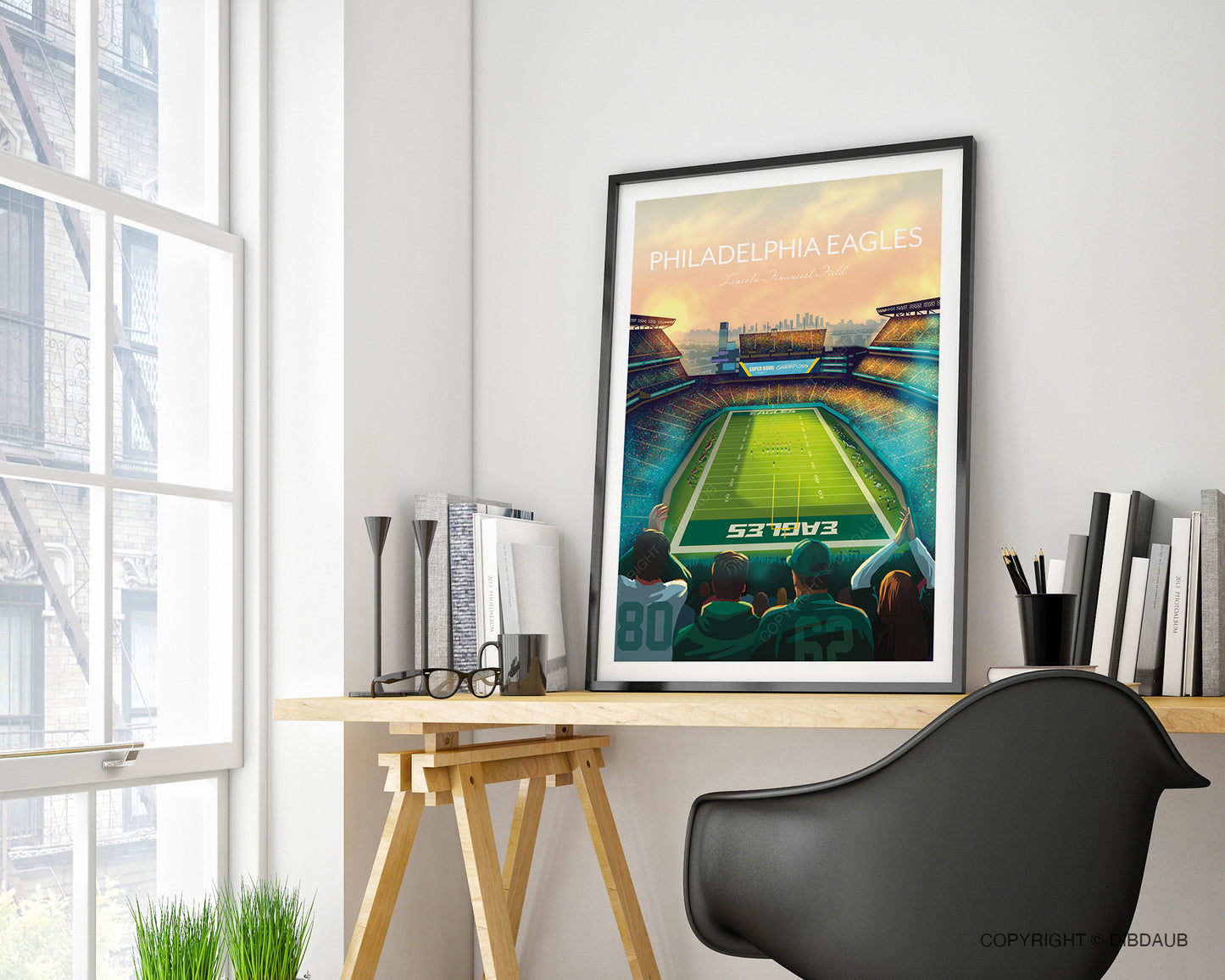 Framed sports art print of a Philadelphia Eagles stadium resting on a home office desk beside a window.