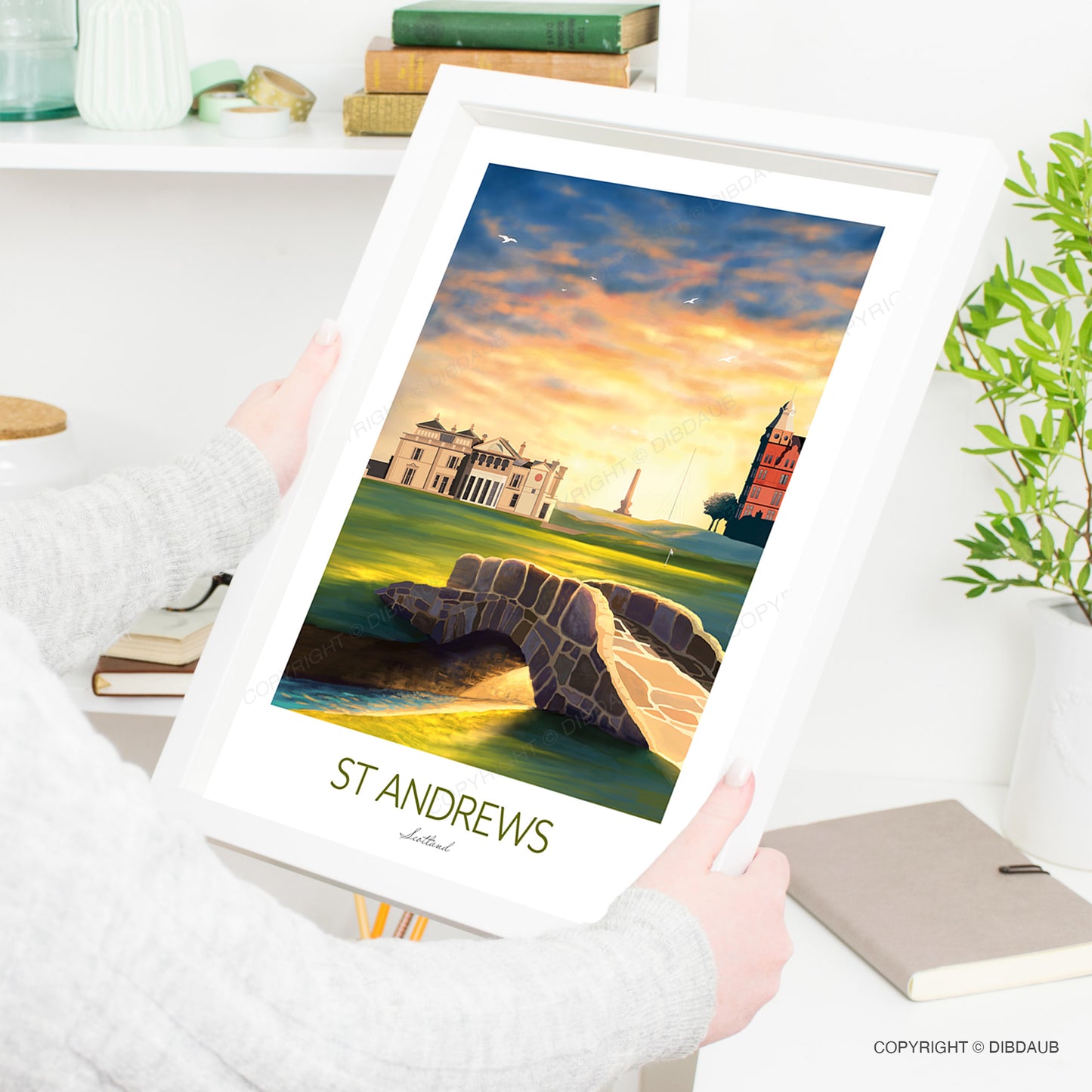 A woman holding a framed golf artwork capturing the atmosphere of the 18th hole at St Andrews Links.