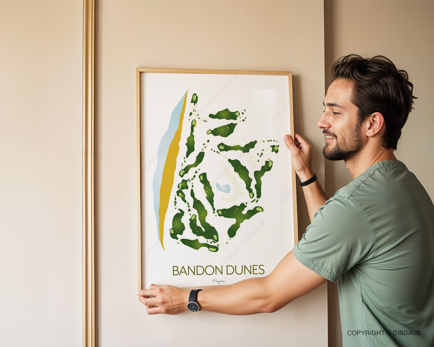 Man hanging a framed golf course map titled 'Bandon Dunes' on a beige wall.