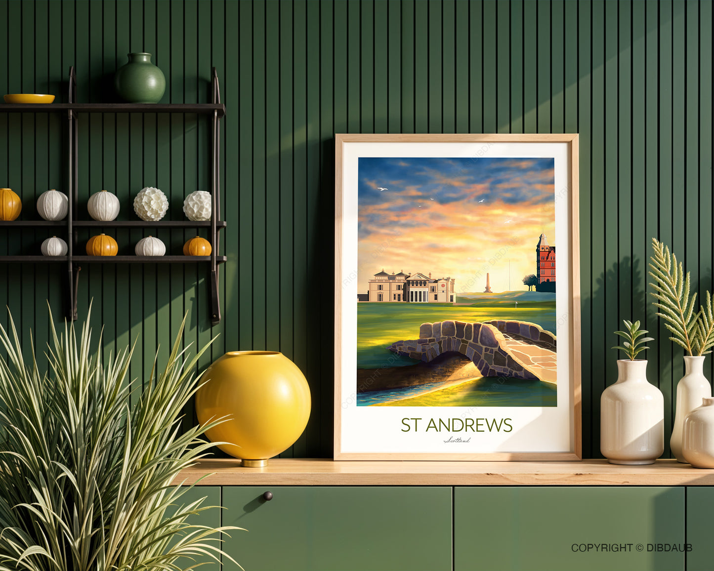 Framed print of St Andrews displayed on a unit with a green wall panelling with decorative items either side.