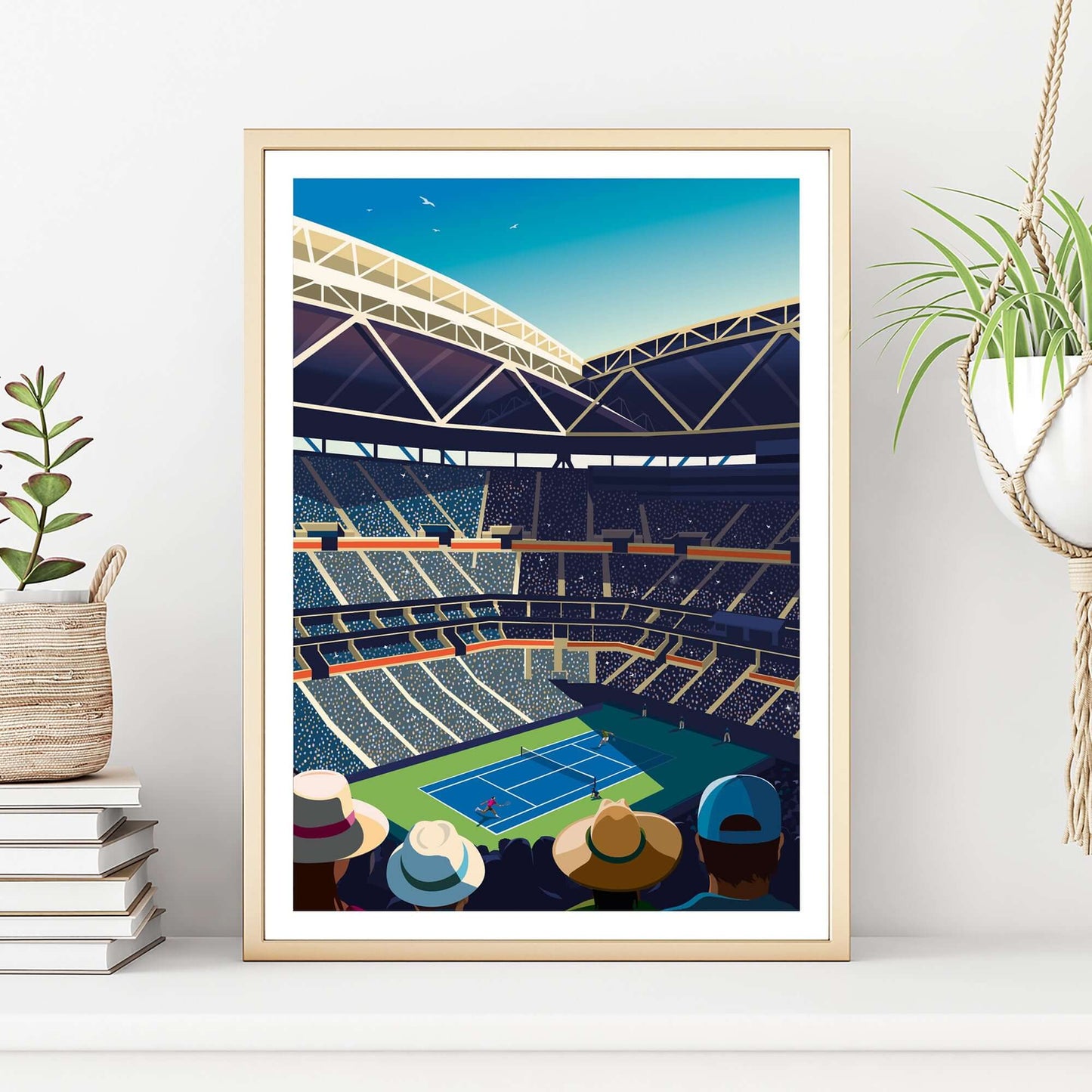 US Open tennis artwork in a gold frame sitting on a sideboard with a hanging plant and books either side.