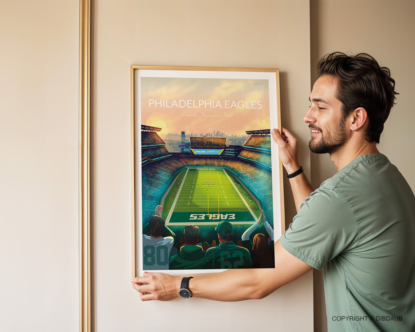 Man hanging a framed artwork of the Eagles Lincoln Financial Field Stadium on a beige wall.