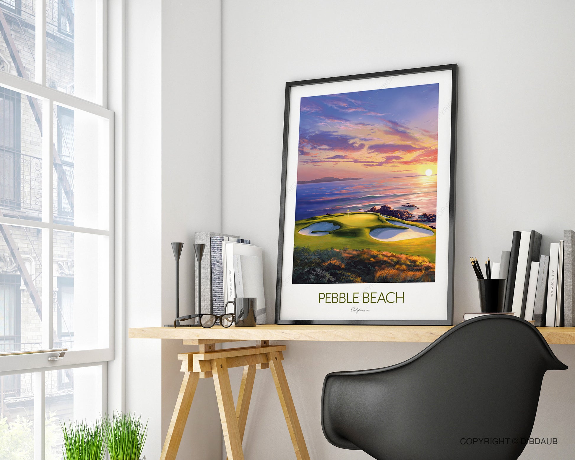 Framed artwork of Pebble Beach sunset golf course on a home office desk with a chair and books.