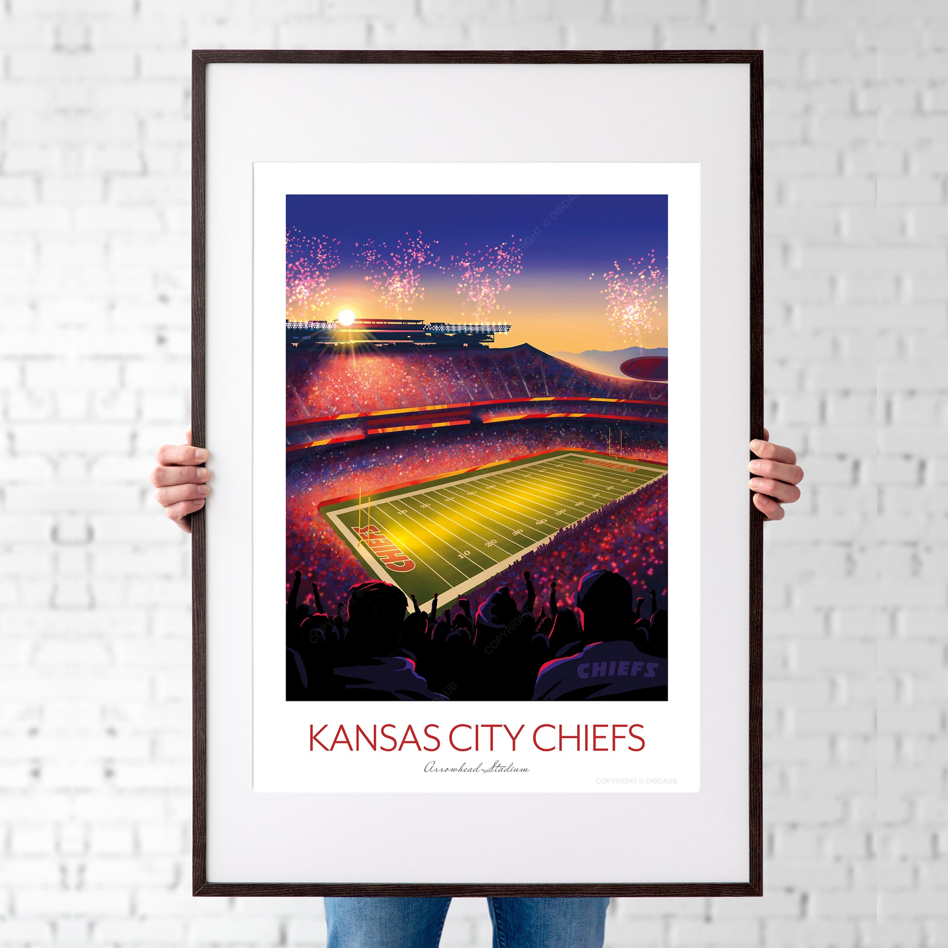 Framed artwork of a football stadium with 'Kansas City Chiefs' text against a white brick wall.