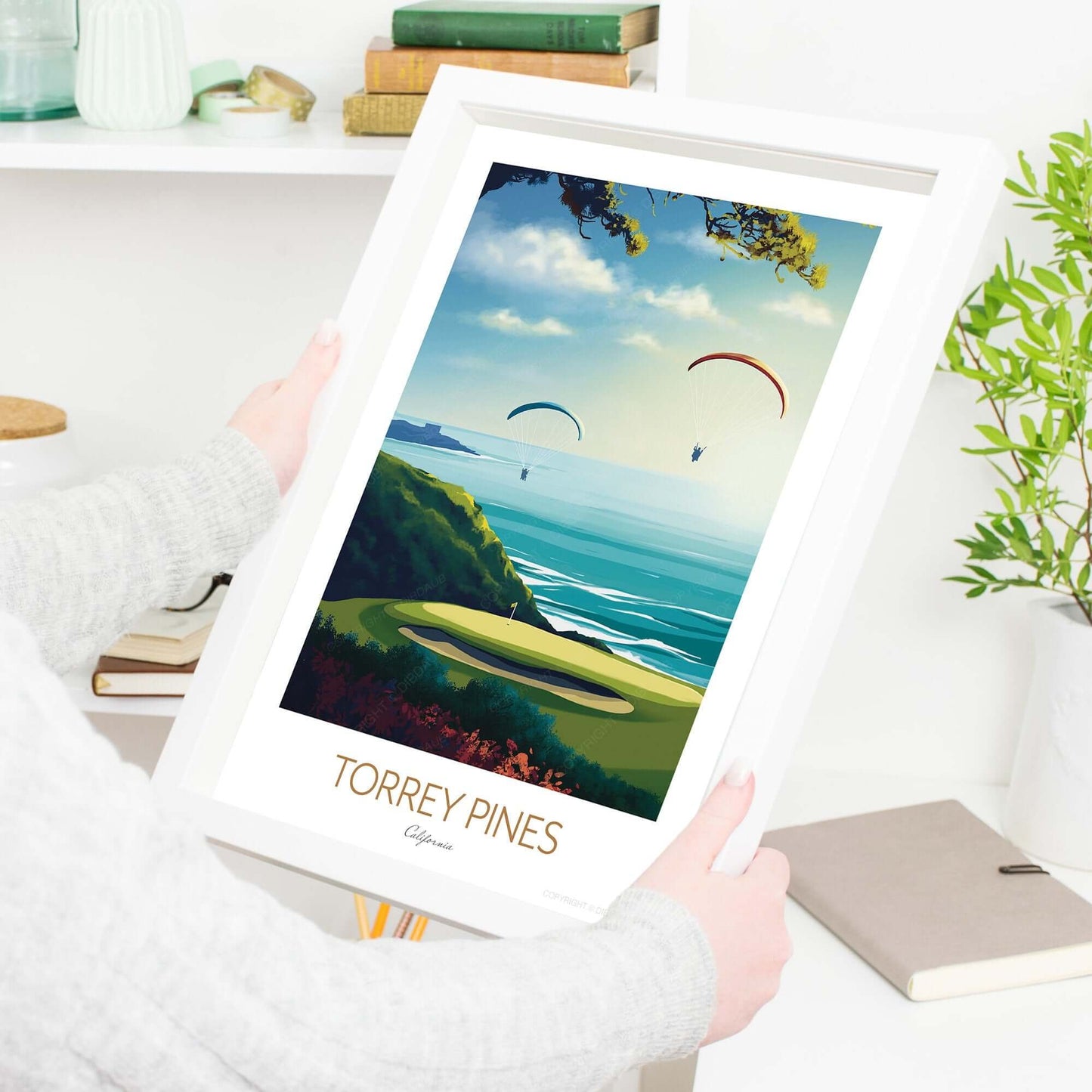 A female holding a framed golf course print of Torrey Pines.