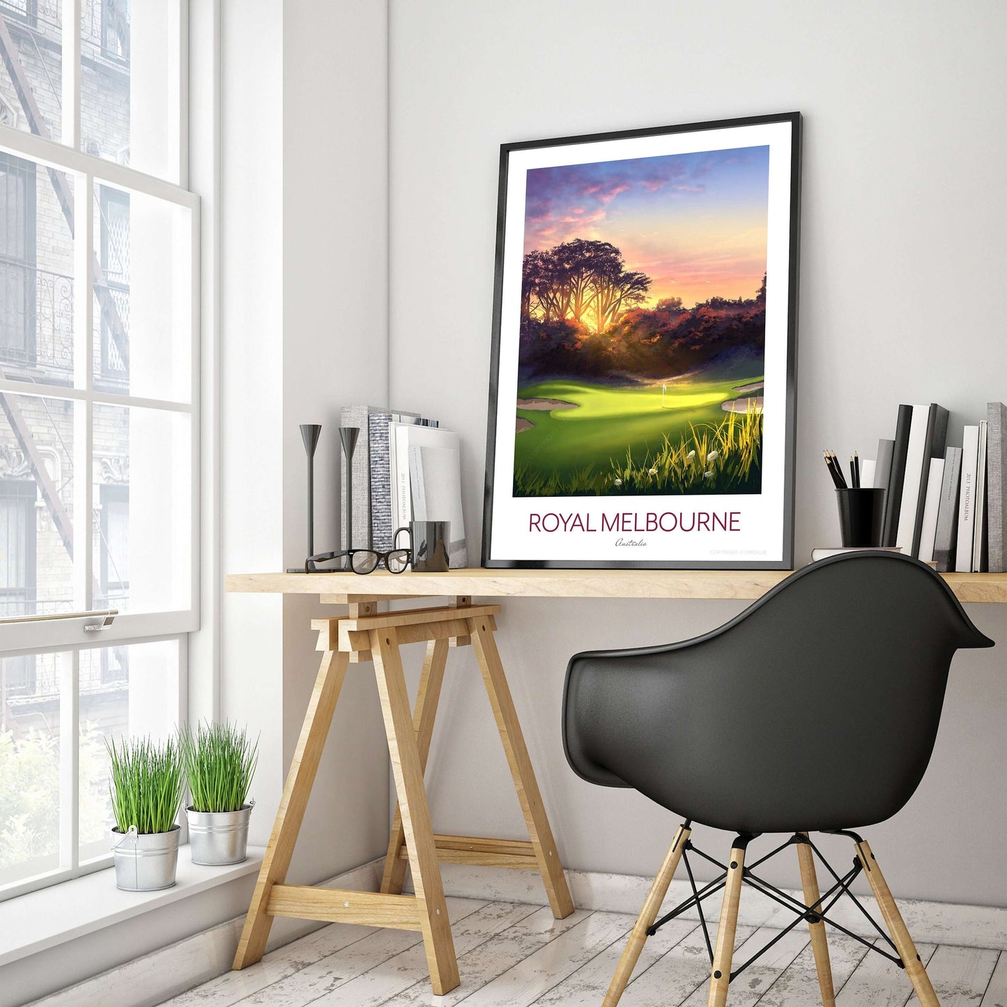 A golf course print of Royal Melbourne West Course 5th hole, with a black frame placed on a office desk.