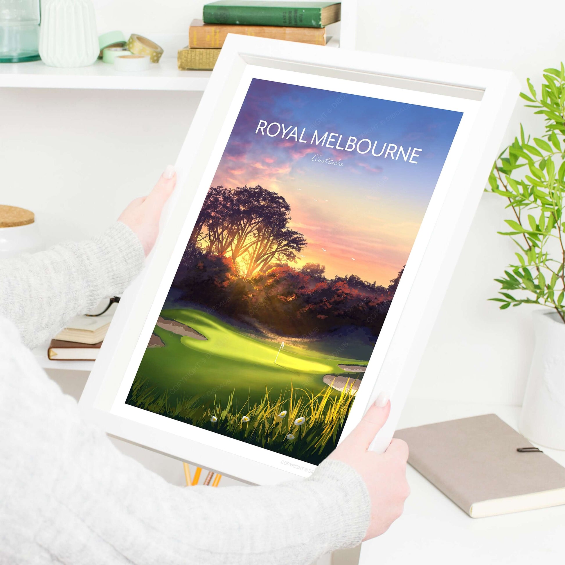 A woman holding a framed golf poster of Royal Melbourne West Course 5th hole.