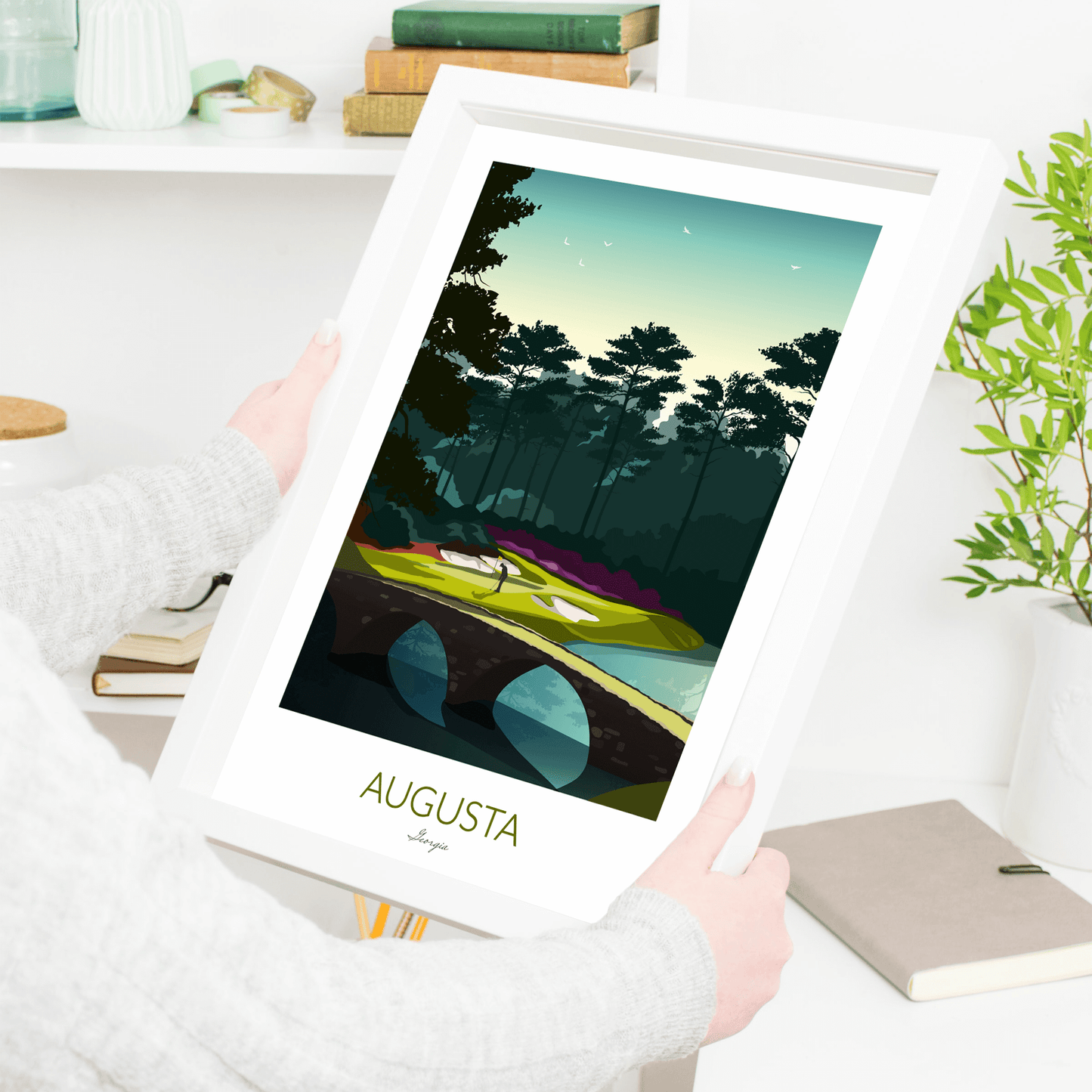 A framed Golf Print of Augusta National being held by a woman beside a book shelf.